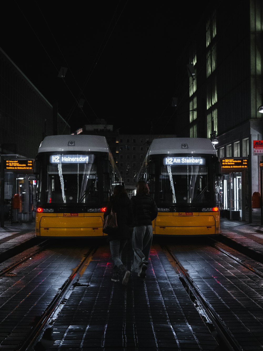 man in black jacket standing beside yellow and black tram during night time