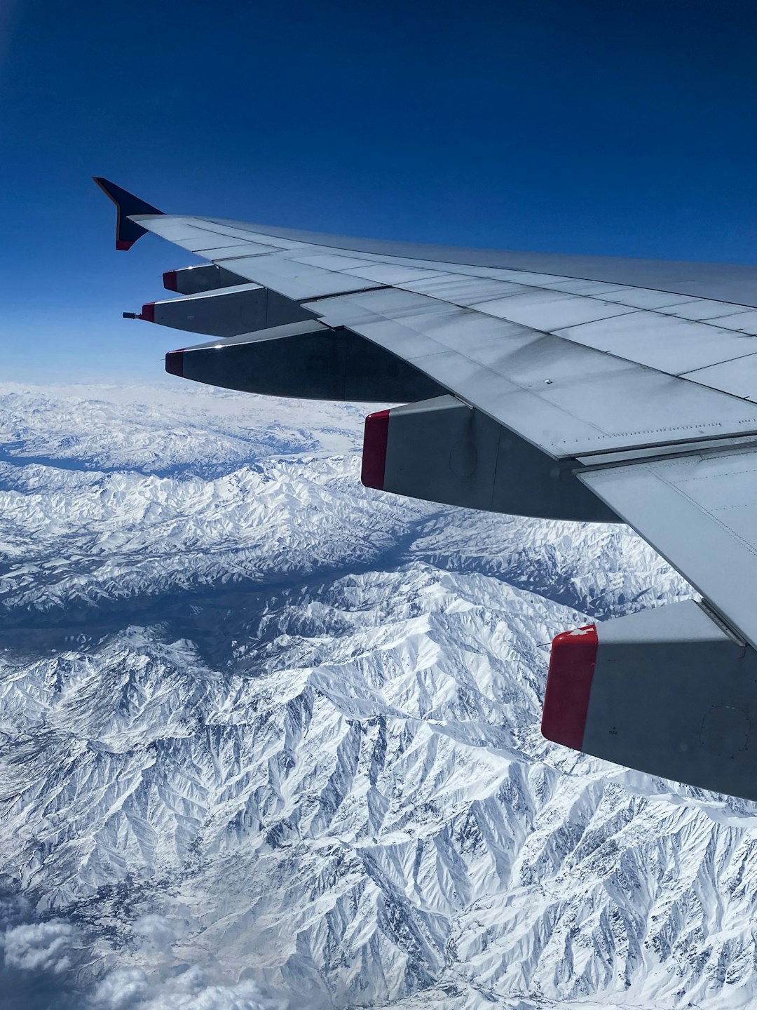 white and red airplane wing over snow covered mountain