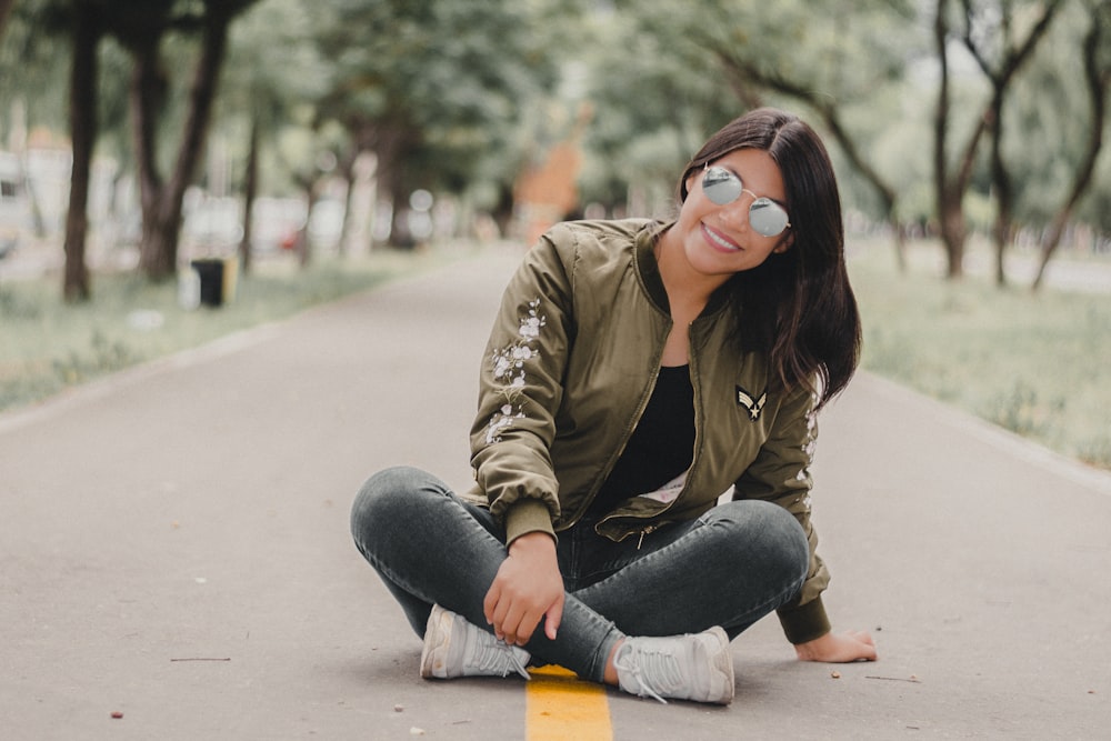 woman in brown jacket and blue denim jeans sitting on gray concrete floor during daytime