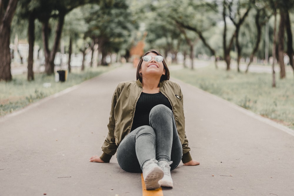 woman in brown jacket and blue denim jeans sitting on the road during daytime