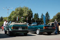 A family happily inspecting a used car outdoors on a sunny day.