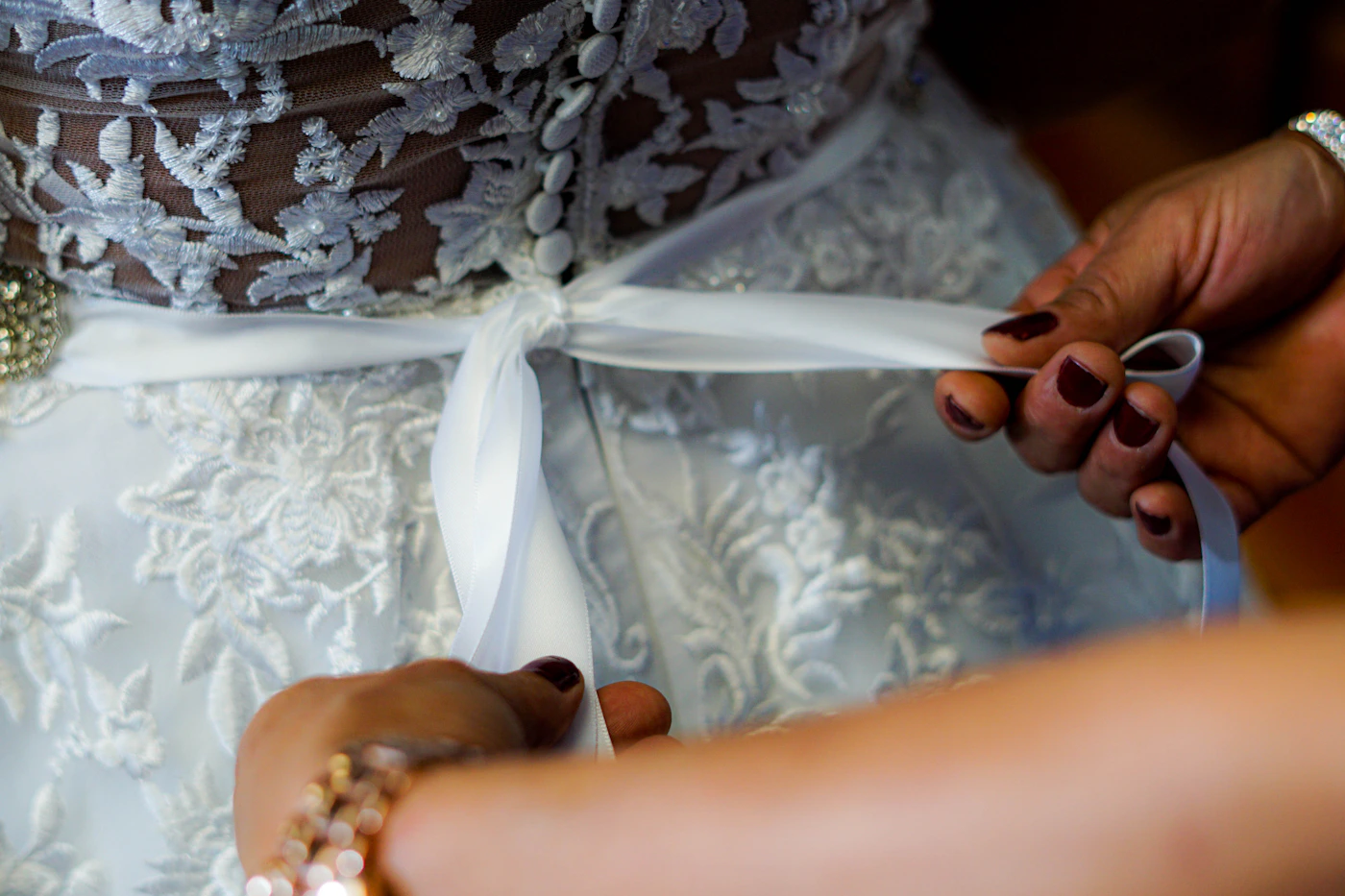 Close-up of bride hands holding white ribbon against white and gray floral fabric, wedding preparation detail photography