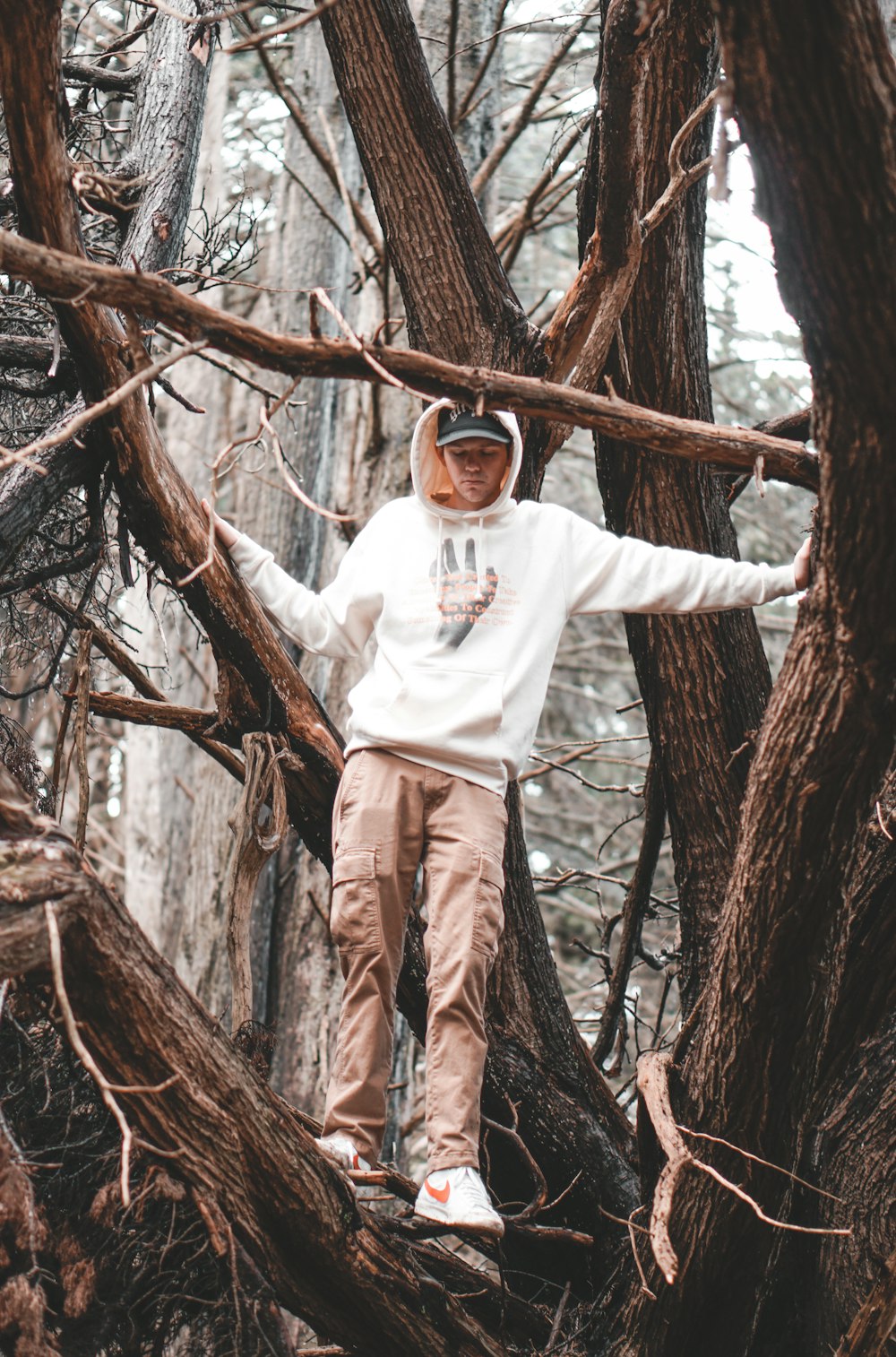 man in white long sleeve shirt and brown pants standing on brown tree branch during daytime