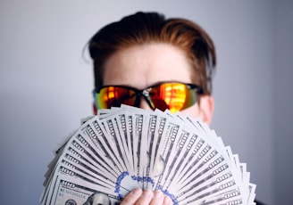 man in black framed sunglasses holding fan of white and gray striped cards