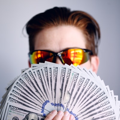 man in black framed sunglasses holding fan of white and gray striped cards