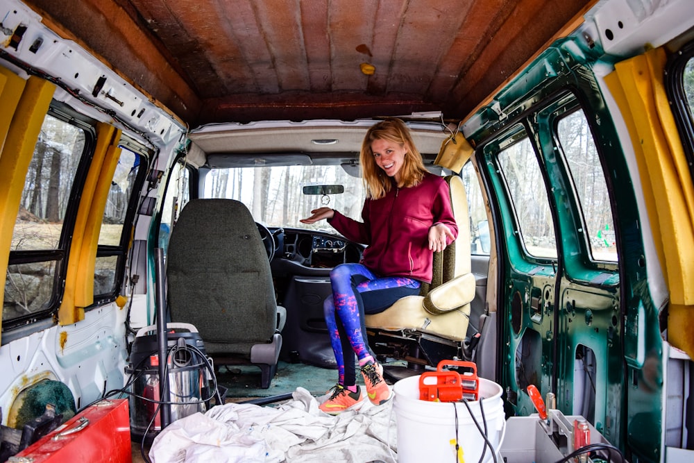 woman in red long sleeve shirt and blue denim jeans sitting on green van