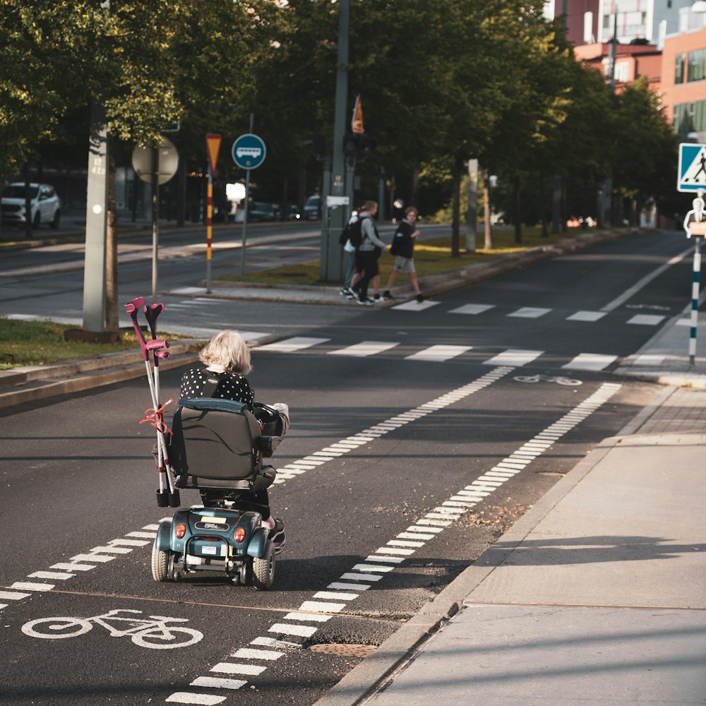 Mädchen in schwarzer Jacke fährt tagsüber auf schwarz-grauem Kinderwagen auf grauer Asphaltstraße