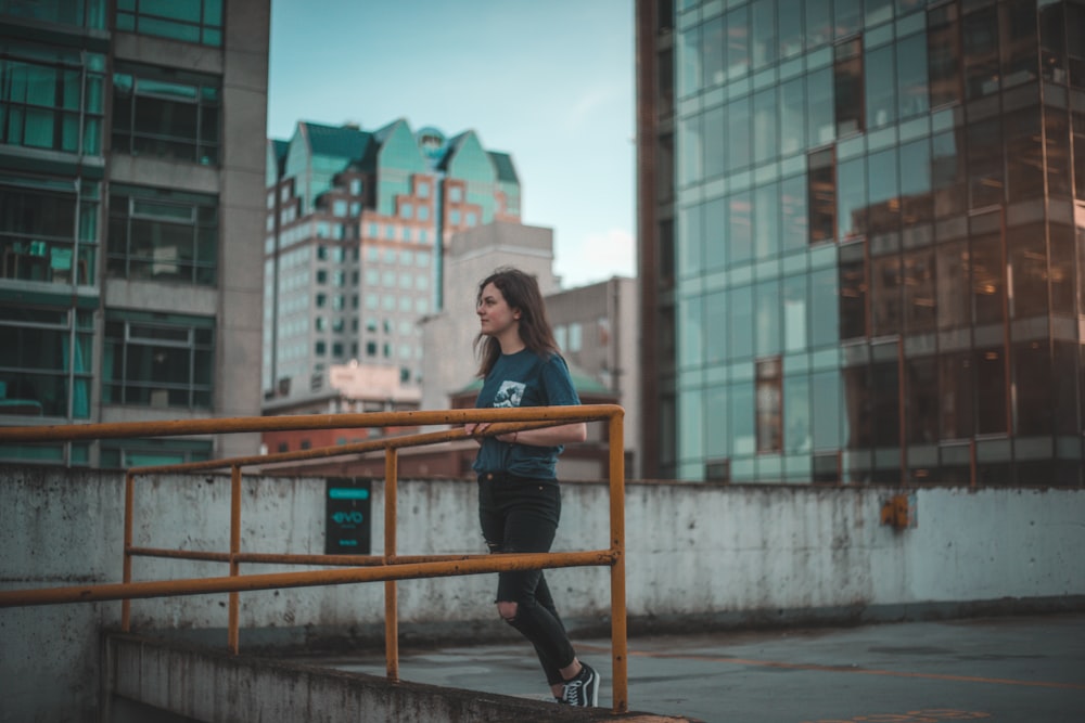 Donna in camicia blu a maniche lunghe e pantaloni neri seduta su una panca di legno marrone durante il giorno