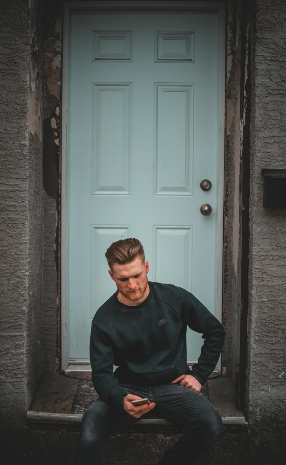 man in blue long sleeve shirt standing beside gray wooden door