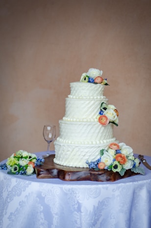 A beautifully decorated three-tier wedding cake with intricate floral designs, placed on a rustic wooden table.