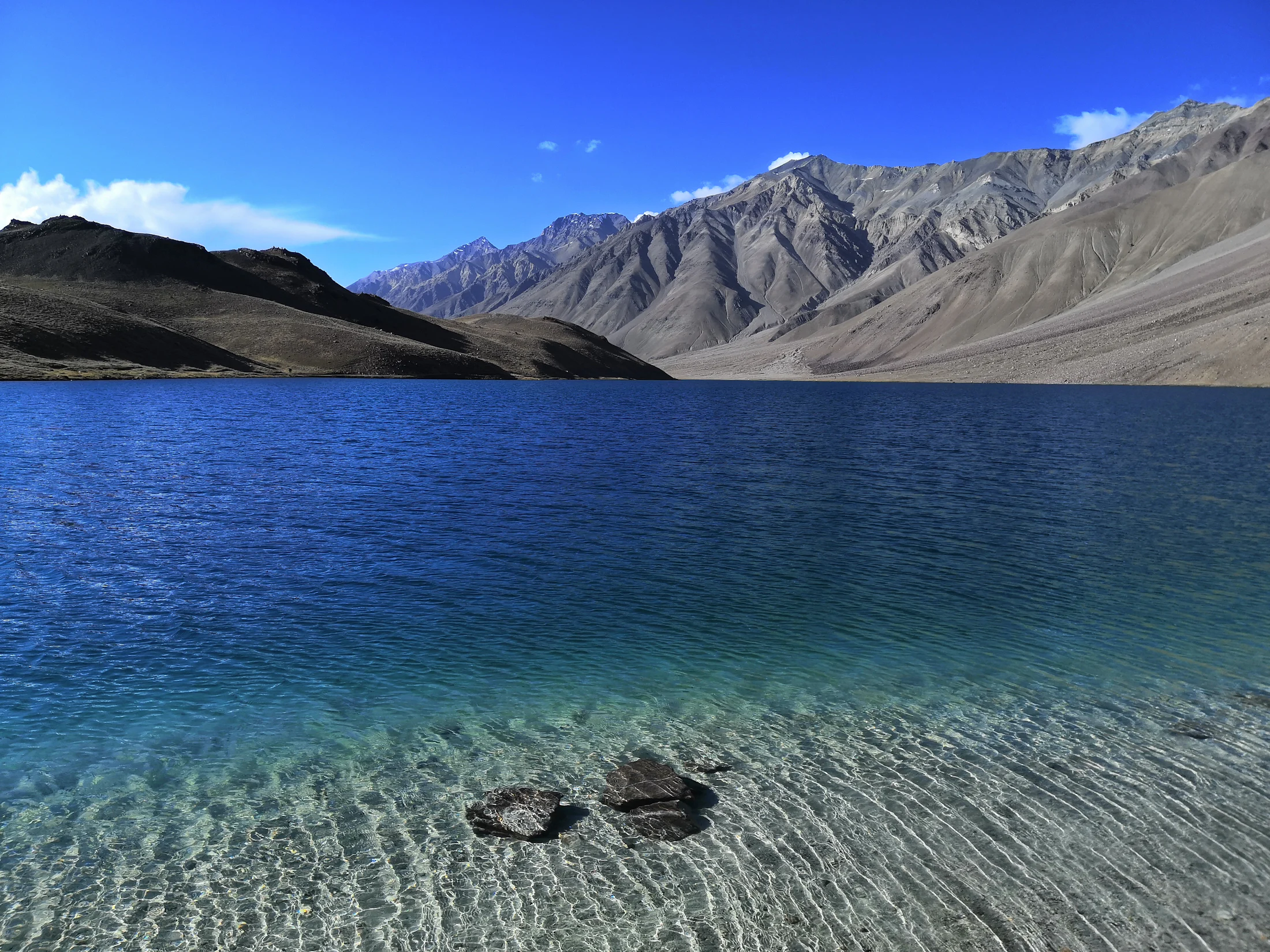 Clear, shallow water of Chandratal lake with bare mountains on the far shore