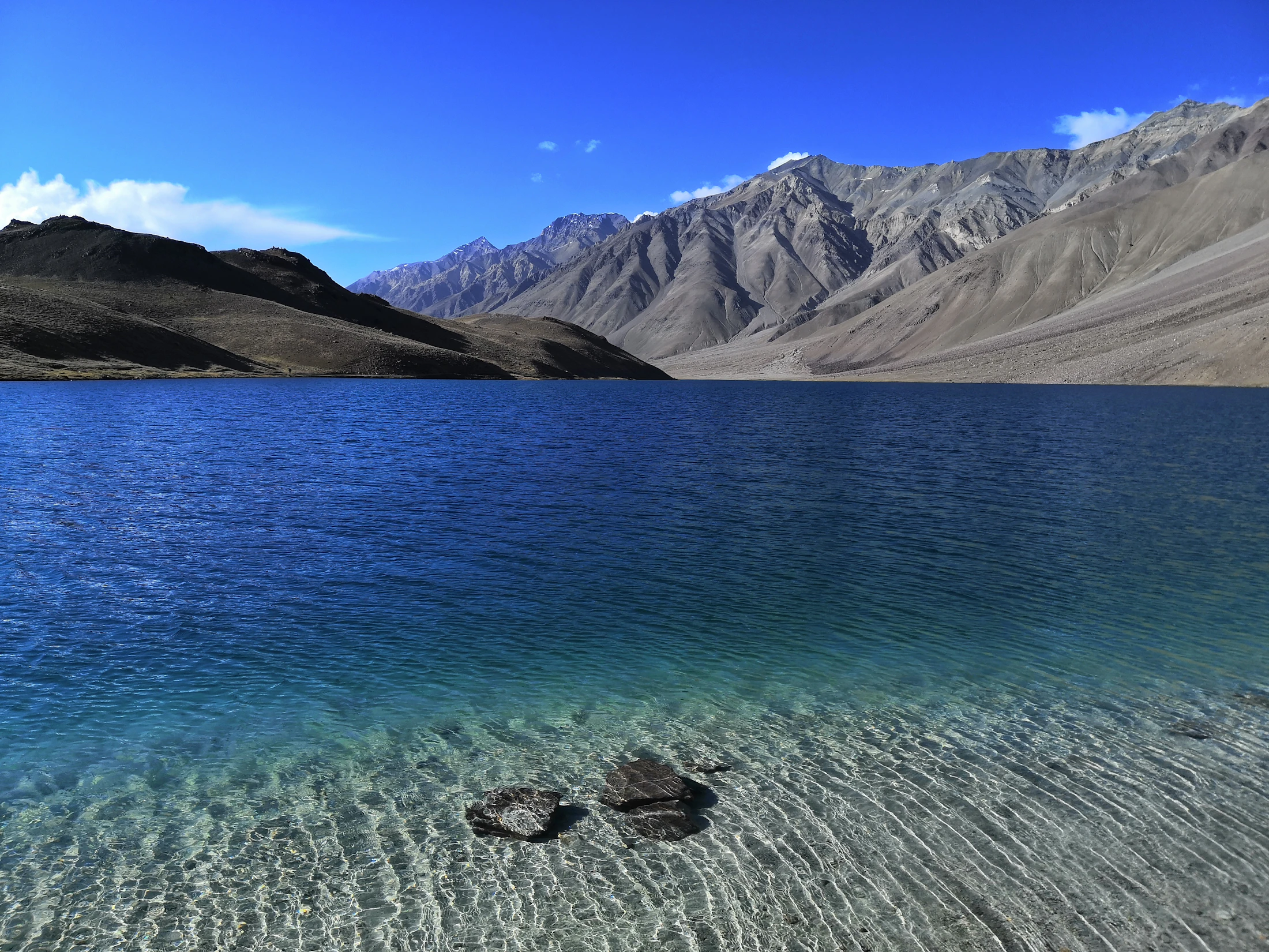 Clear, shallow water of Chandratal lake with bare mountains on the far shore