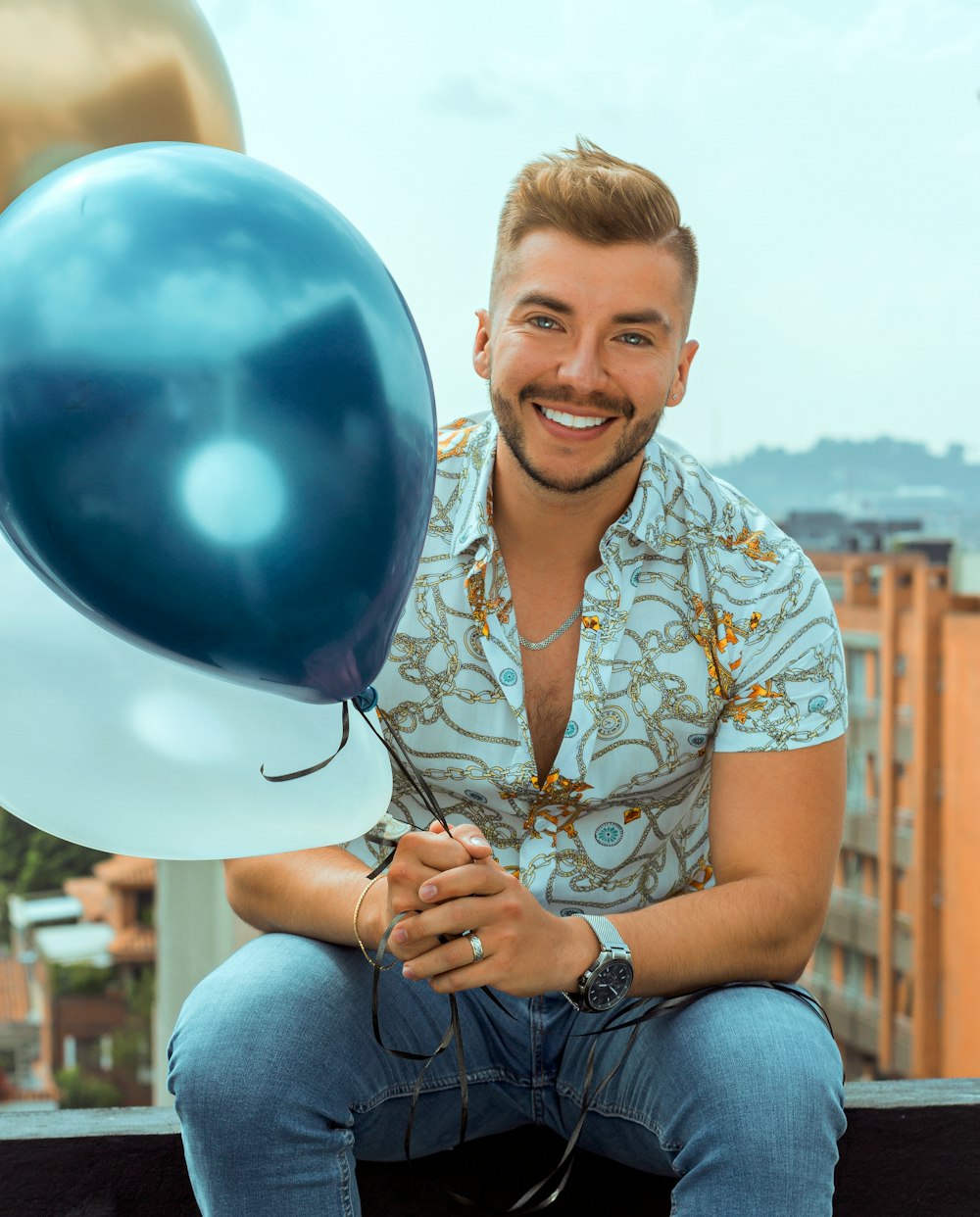 smiling man in blue and white floral button up shirt holding blue balloons
