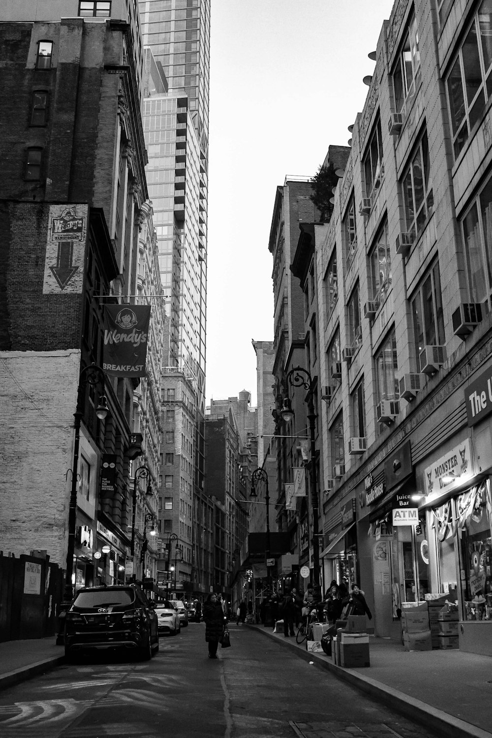 grayscale photo of people walking on street between buildings