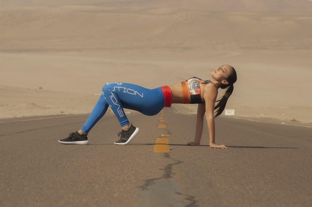 Donna in reggiseno sportivo rosso e leggings blu che fa yoga su sabbia grigia durante il giorno