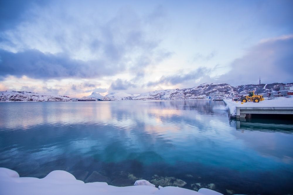 white and black house on snow covered ground near body of water under white clouds and