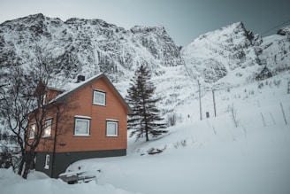 A cozy prefabricated cottage nestled on a snowy mountain slope with burnt orange accents.