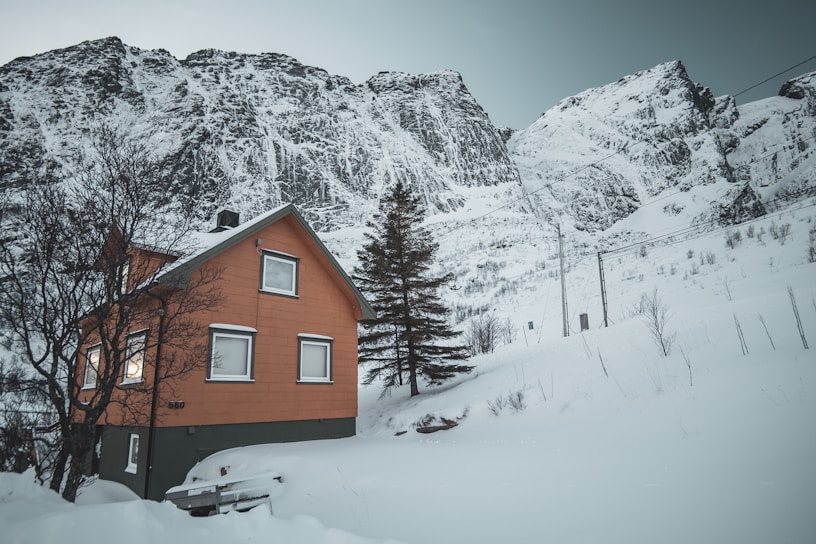A cozy prefabricated cottage nestled on a snowy mountain slope with burnt orange accents.