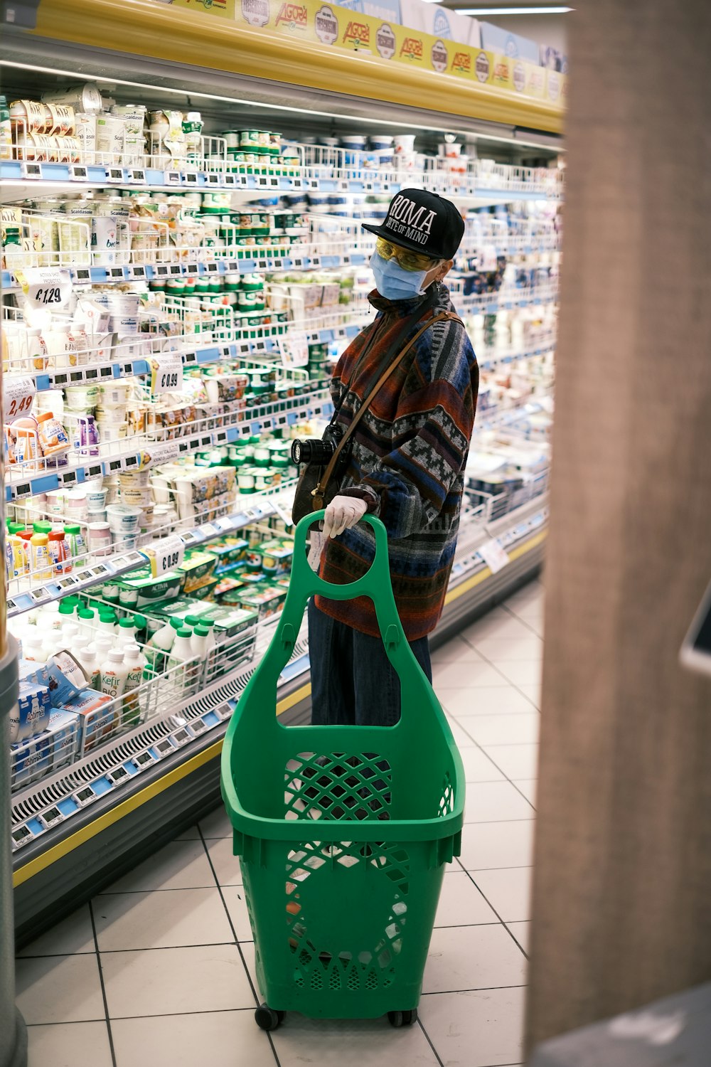 Mujer en chaqueta marrón y negro sosteniendo la cesta de la compra de plástico verde