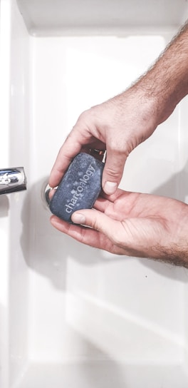 A rugged man washing his hands with a bar of Gentle Grizzly soap outdoors, surrounded by nature.