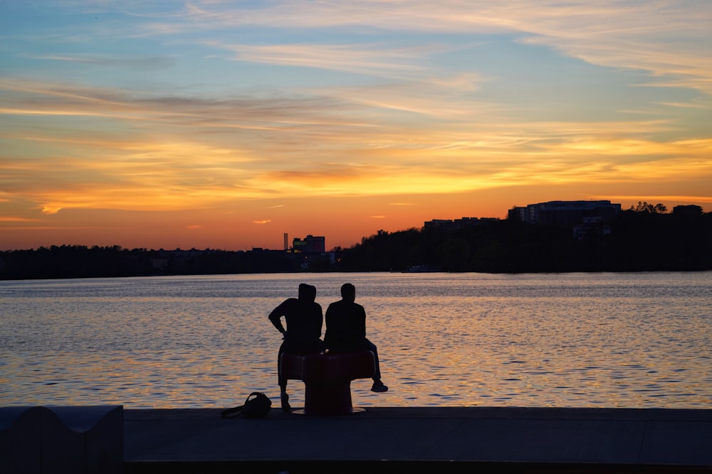 silhouette of man and woman sitting on dock during sunset