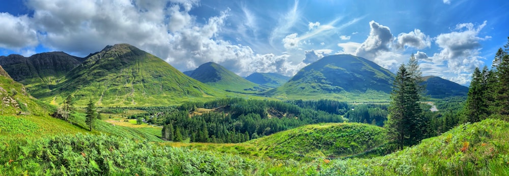 Grünes Grasfeld und grüne Berge unter blauem Himmel und weißen Wolken tagsüber