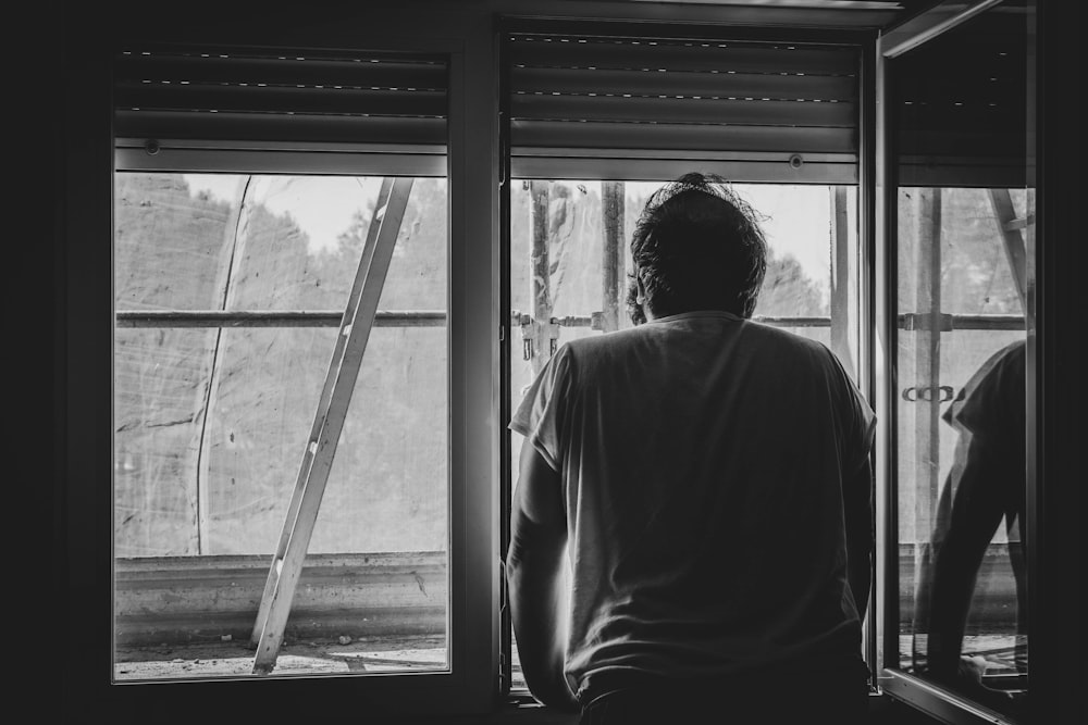 grayscale photo of man in white shirt standing near window