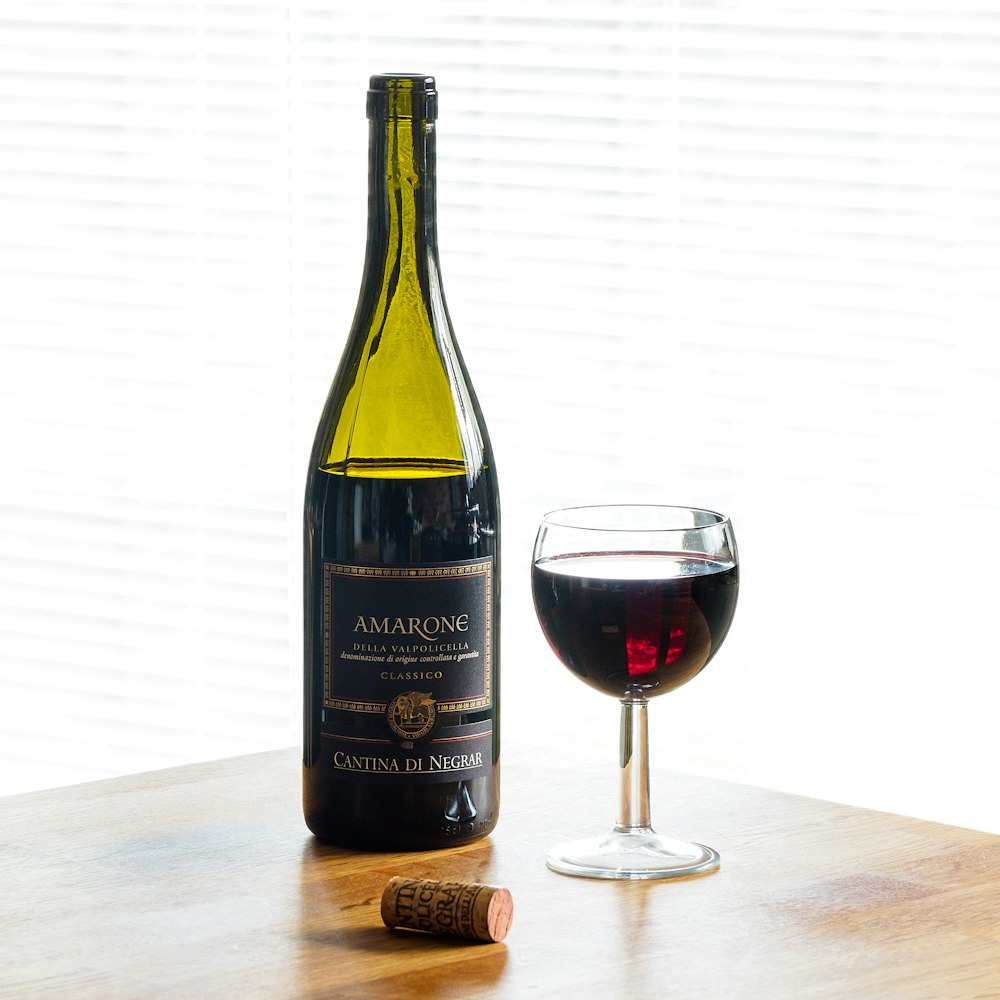 black wine bottle beside clear wine glass on brown wooden table