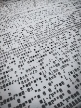 Rows of distorted, random, and overlapping characters and symbols in black on a white background create a chaotic pattern.
