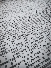 Rows of distorted, random, and overlapping characters and symbols in black on a white background create a chaotic pattern.