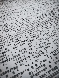 Rows of distorted, random, and overlapping characters and symbols in black on a white background create a chaotic pattern.