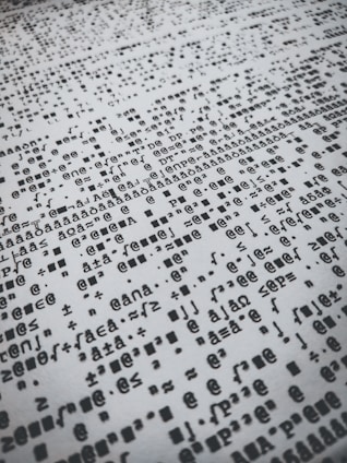 Rows of distorted, random, and overlapping characters and symbols in black on a white background create a chaotic pattern.
