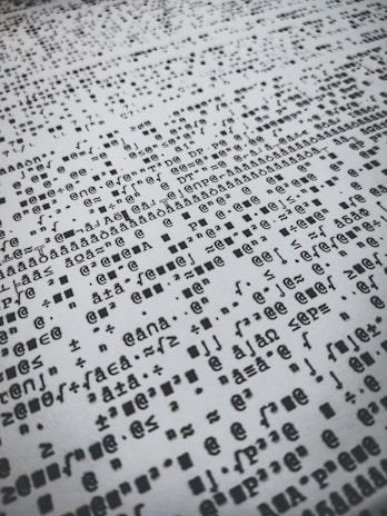 Rows of distorted, random, and overlapping characters and symbols in black on a white background create a chaotic pattern.