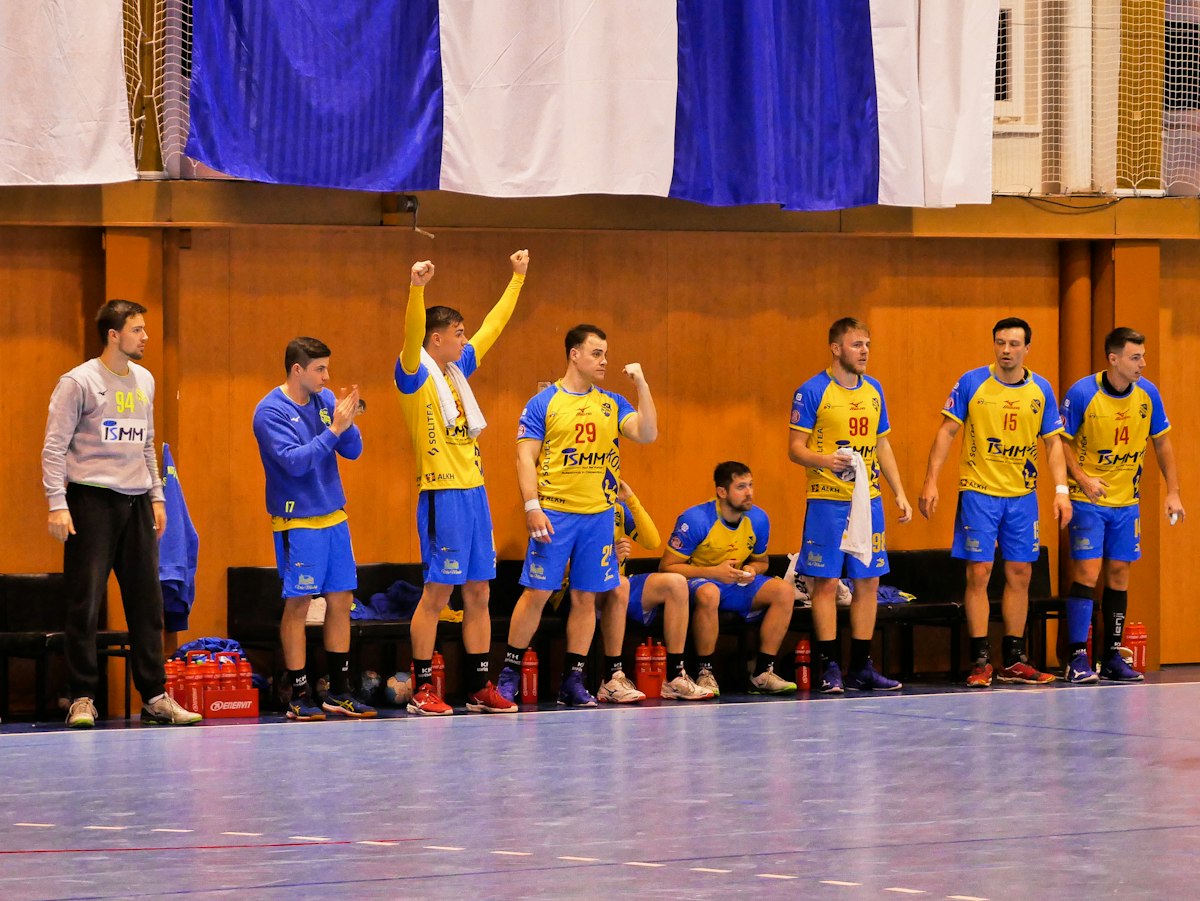 Banc d'une équipe de handball en maillots jaunes qui célèbre debout, bras levés