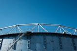 A large industrial structure with a series of triangular metal supports and a ladder leading to the top. The structure is painted blue and the background is a clear sky.