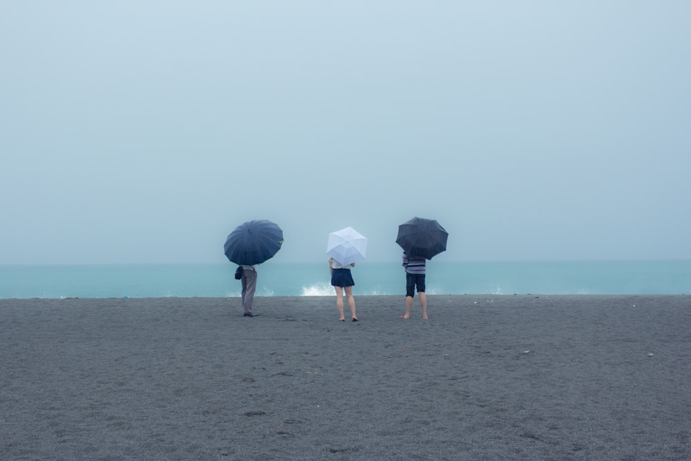 woman in white dress holding black umbrella walking on beach during daytime