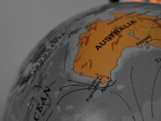 A close-up view of a globe highlighting Australia in orange, with surrounding areas in muted grayscale. The names of cities like Perth, Fremantle, Albany, and Adelaide are visible, along with parts of the Indian Ocean.