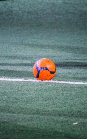 A vibrant photo of a soccer ball resting on lush green grass under stadium lights at dusk.