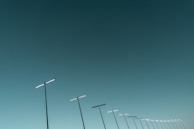 Futuristic solar street light poles aligned along an urban street, casting sharp shadows.