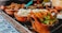 A variety of traditional Mexican dishes on a tray, placed on a decorative tiled table. Clay bowls are filled with ingredients such as shredded cabbage and colorful squash blossoms, accompanied by other items like seasoned meat and sauces. The vivid colors and textures contribute to an inviting and vibrant presentation.