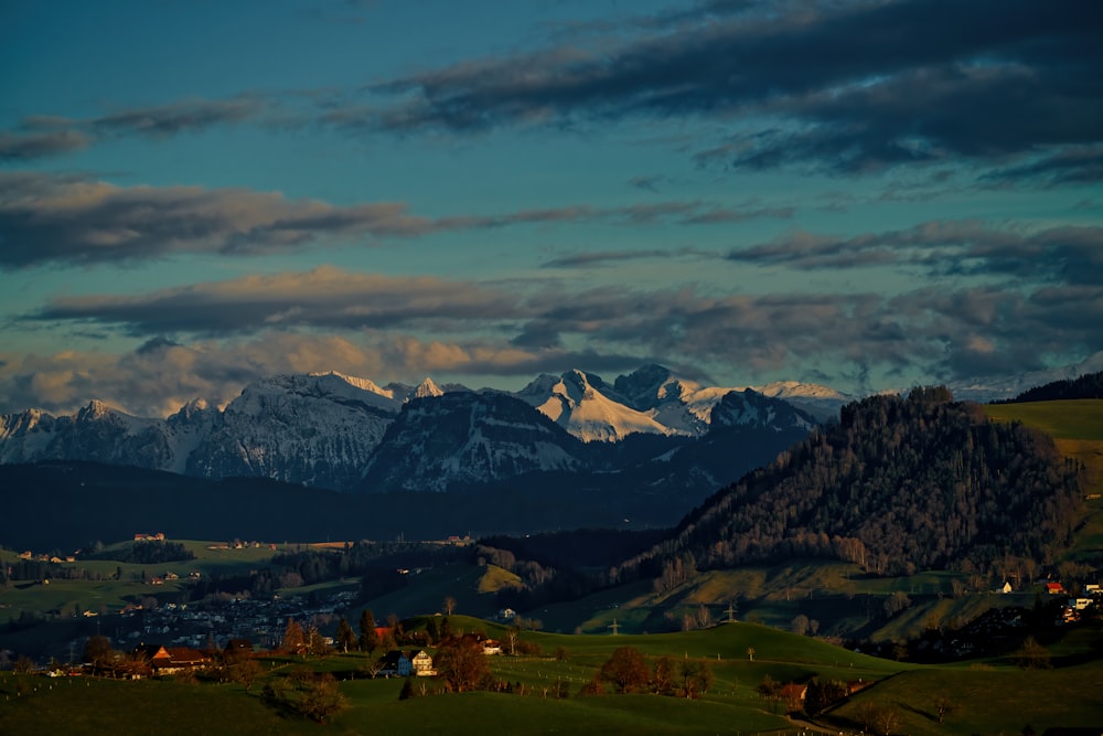 green grass field near mountain under cloudy sky during daytime