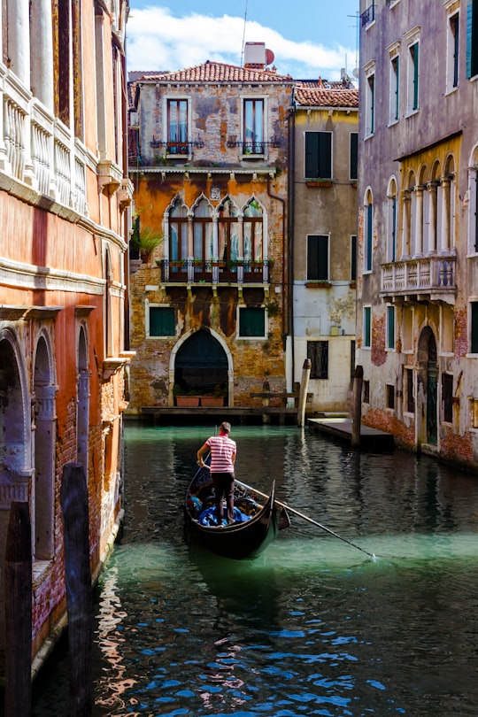 man in black and white boat on river between concrete buildings during daytime in Gondola Italy