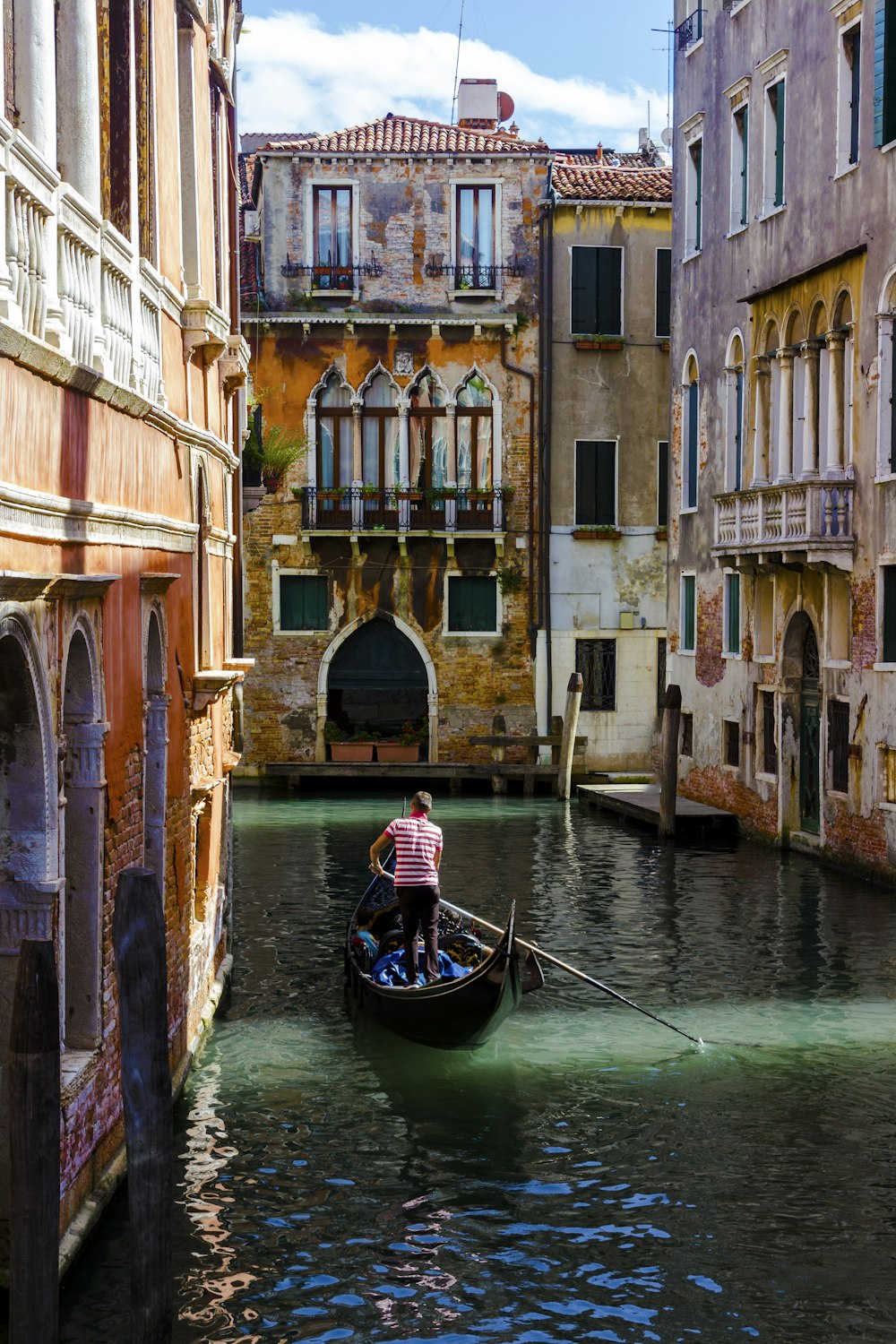 man in black and white boat on river between concrete buildings during daytime