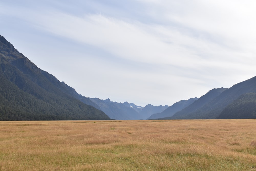 green grass field near mountain under white clouds during daytime