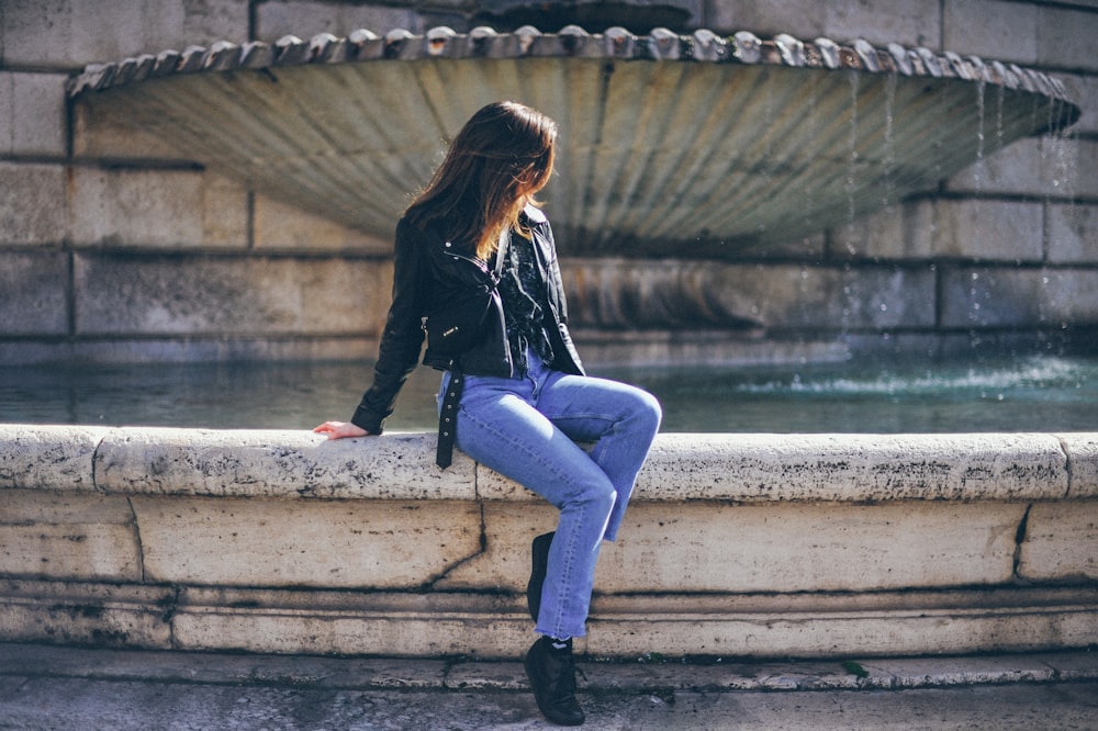 Mujer con chaqueta de cuero negra y jeans de mezclilla azul sentada en una escalera de concreto