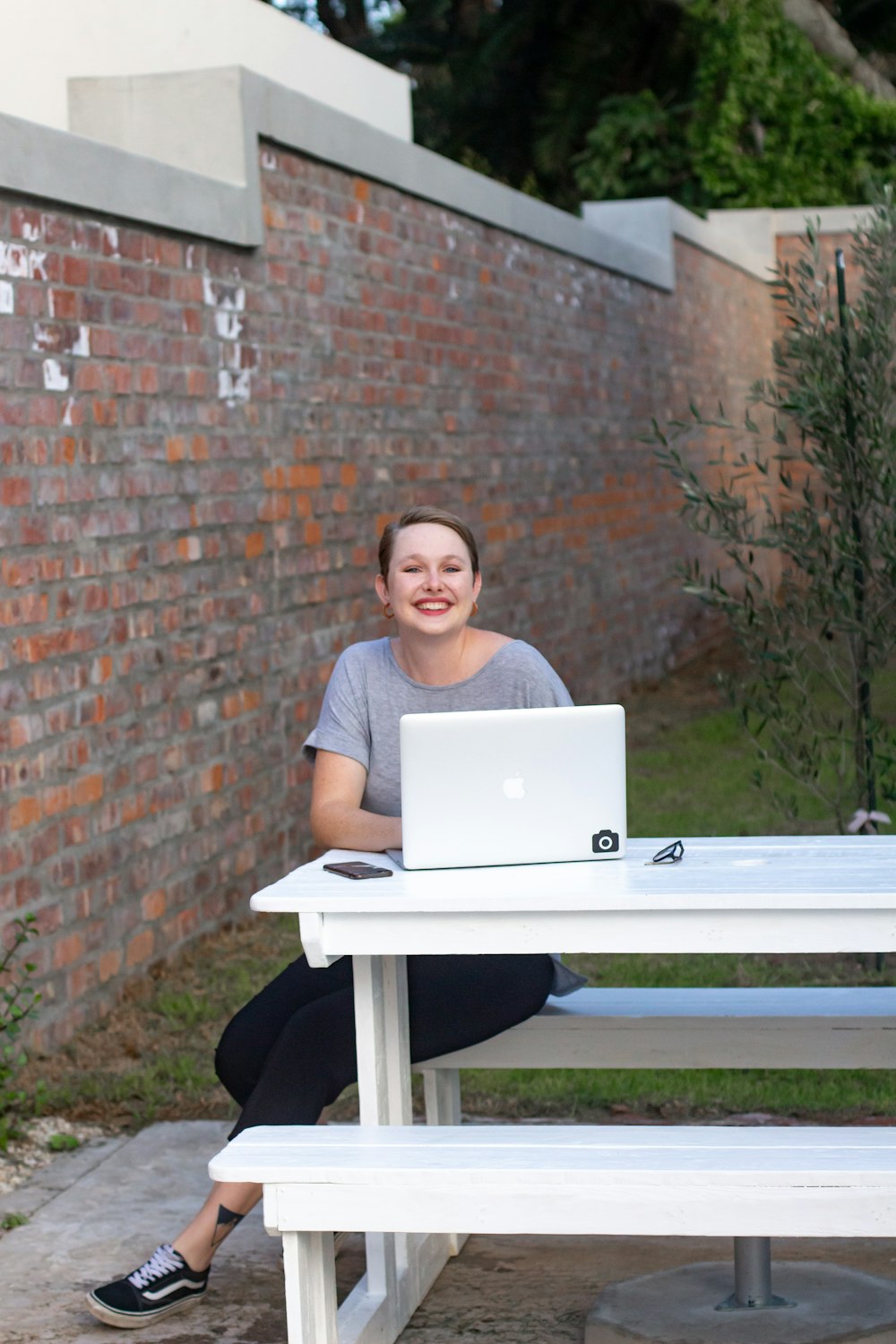 Femme en chemise noire assise sur une table blanche à l’aide d’un MacBook argenté