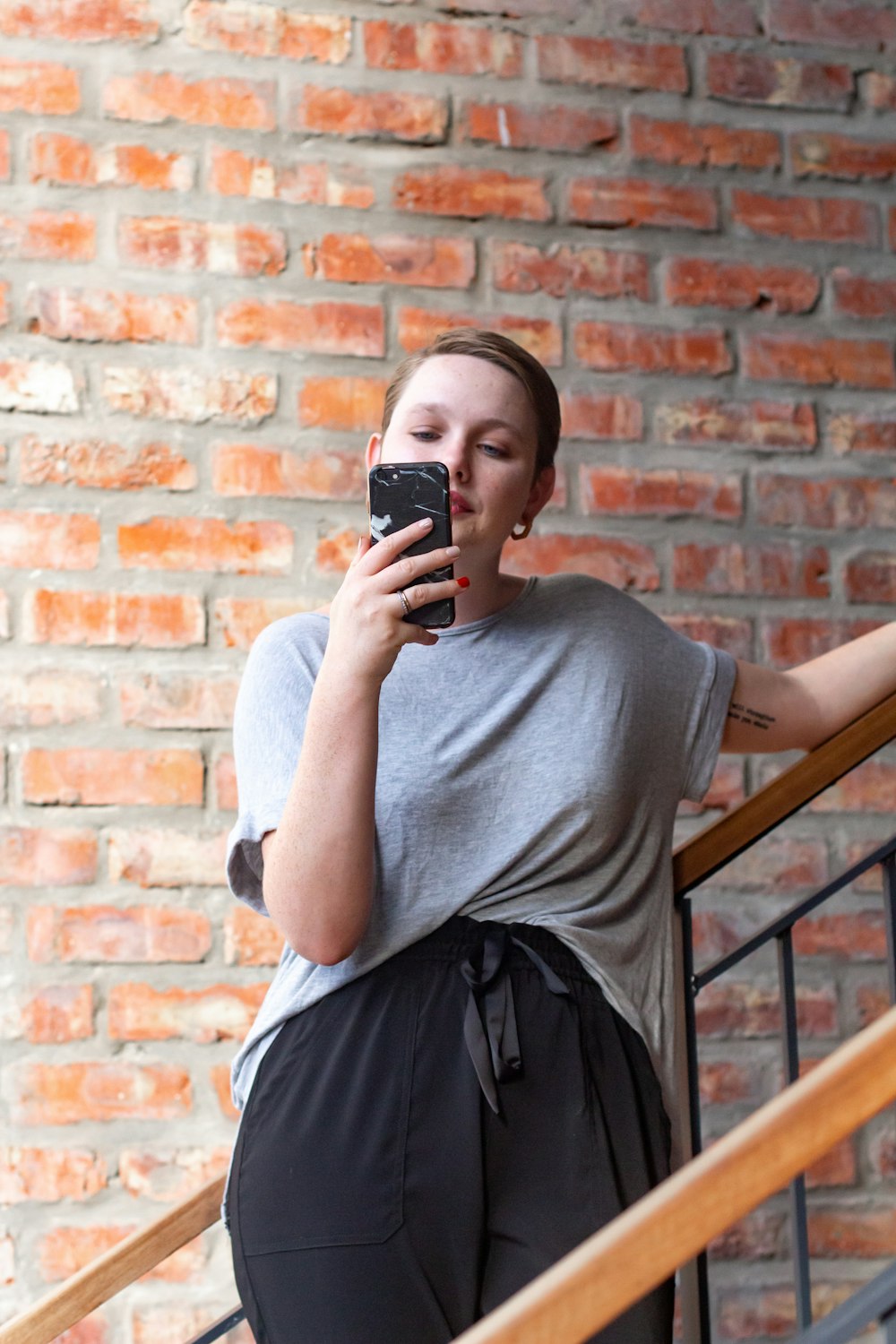 Femme en t-shirt gris à col rond et jupe noire tenant un smartphone noir
