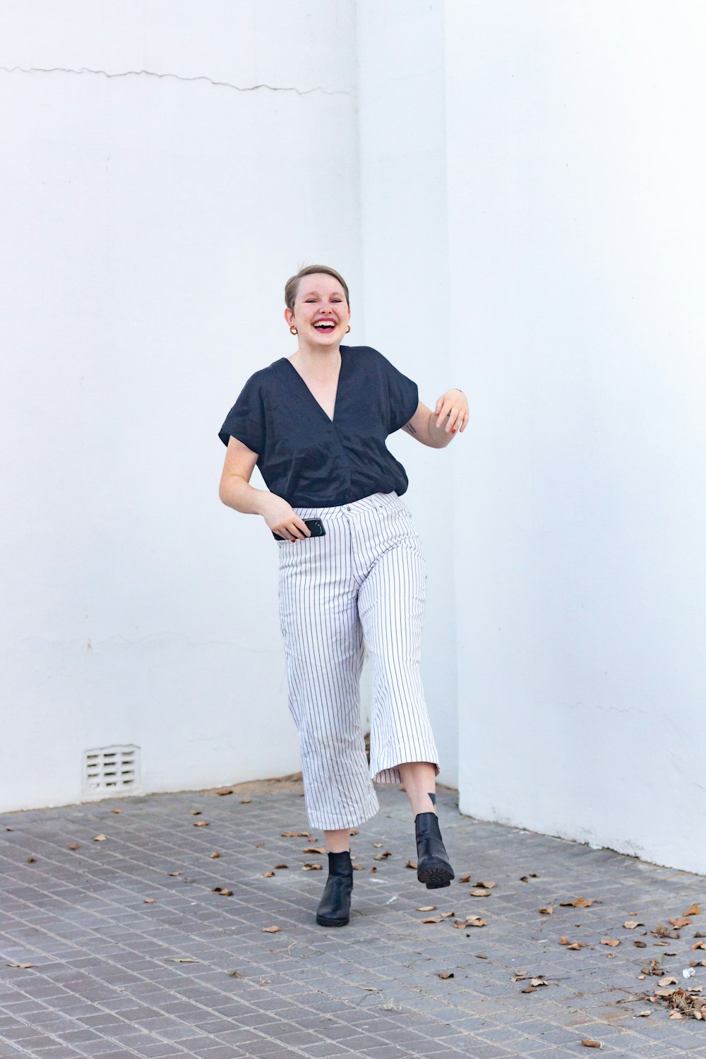 woman in black v neck shirt and white and black striped pants standing beside white painted