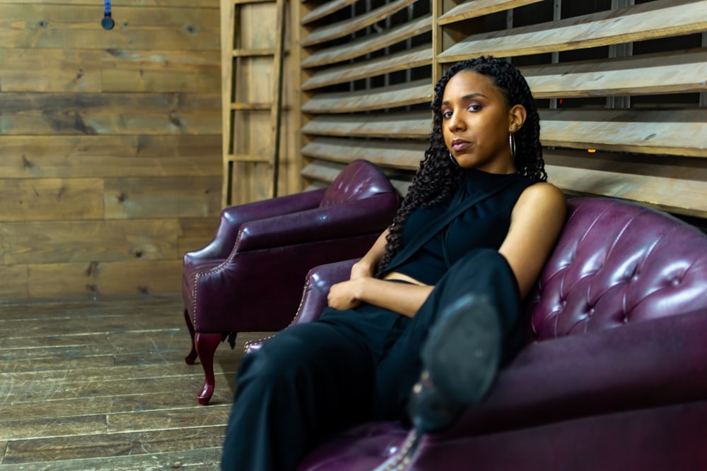 woman in black sleeveless dress sitting on red leather couch