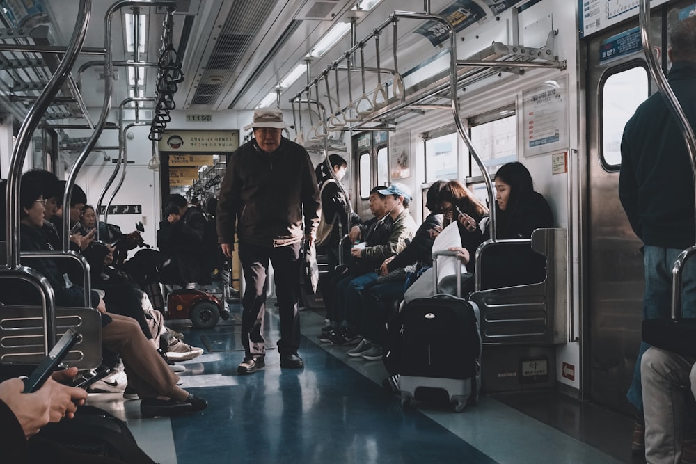 man in black jacket standing beside people sitting on train
